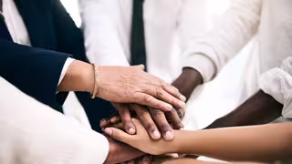 Foto: Mehrere Personen stehen in einem kleinen Kreis, in der Mitte legen sie ihre Hände übereinander.