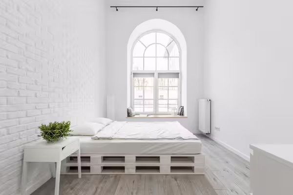 Ein helles, minimalistisches Schlafzimmer mit hohen weißen Wänden und einer großen, bogenförmigen Fensterfront.