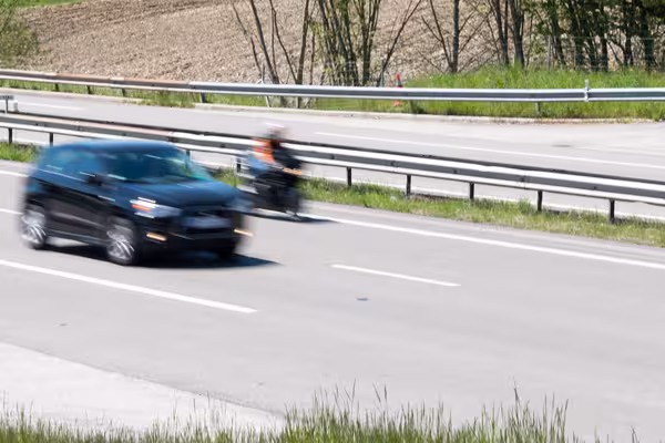Vorbeifahrendes Auto und Motorrad auf einer Landstraße, beide in Bewegungsunschärfe.