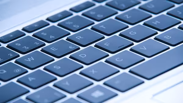 Nahaufnahme einer Computer-Tastatur mit dunkelgrauen und schwarzen Tasten. Die Buchstaben und Zeichen sind klar erkennbar, die Perspektive zeigt die Tasten schräg von oben. Die Oberfläche wirkt modern und glatt.