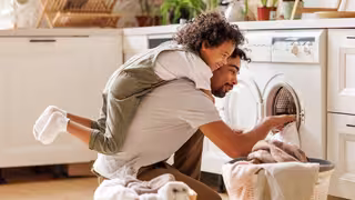 Vater und Sohn sitzen vor der Waschmaschine und befüllen diese mit Wäsche.